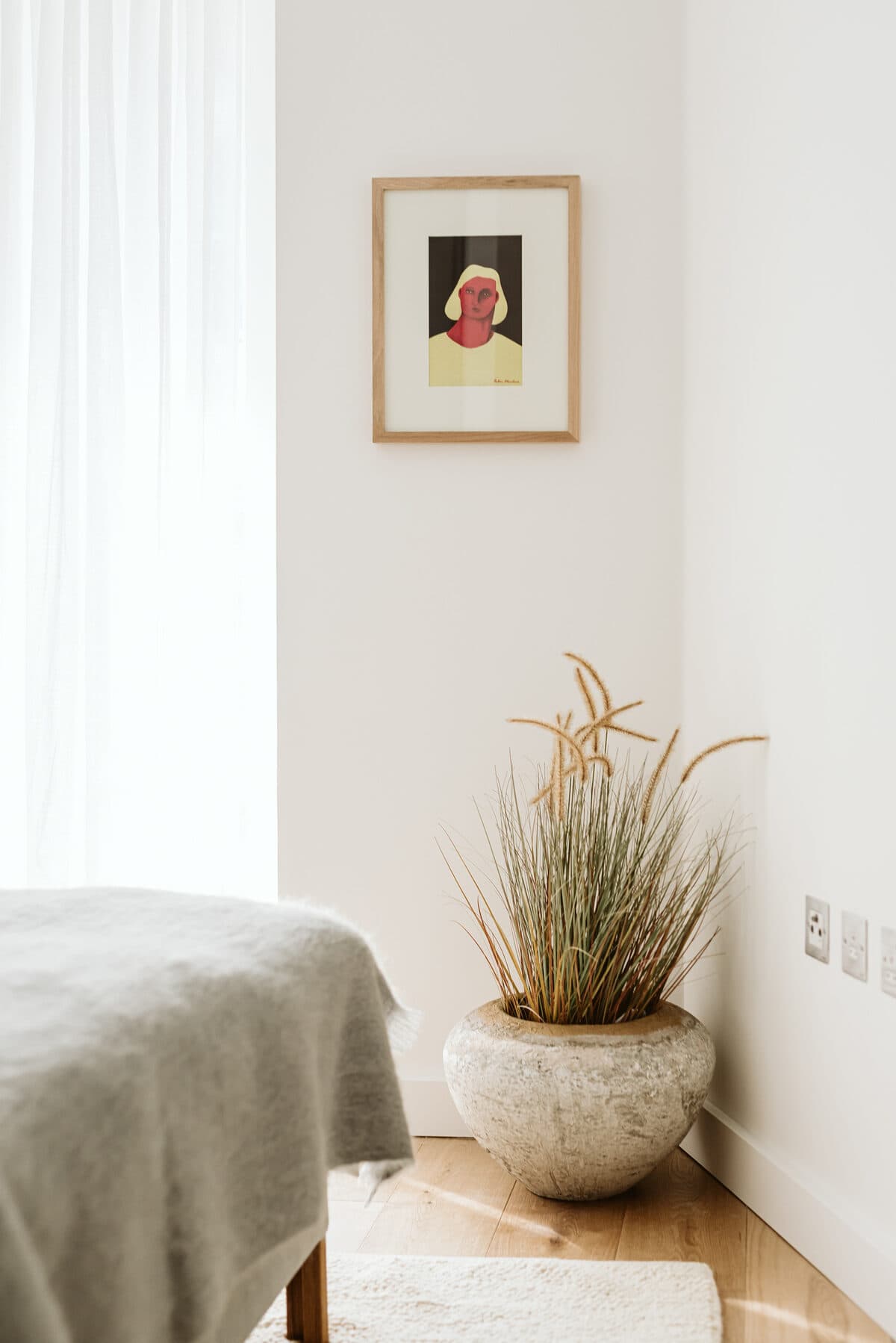 Bedroom corner with stone planter, framed portrait art and natural linen
